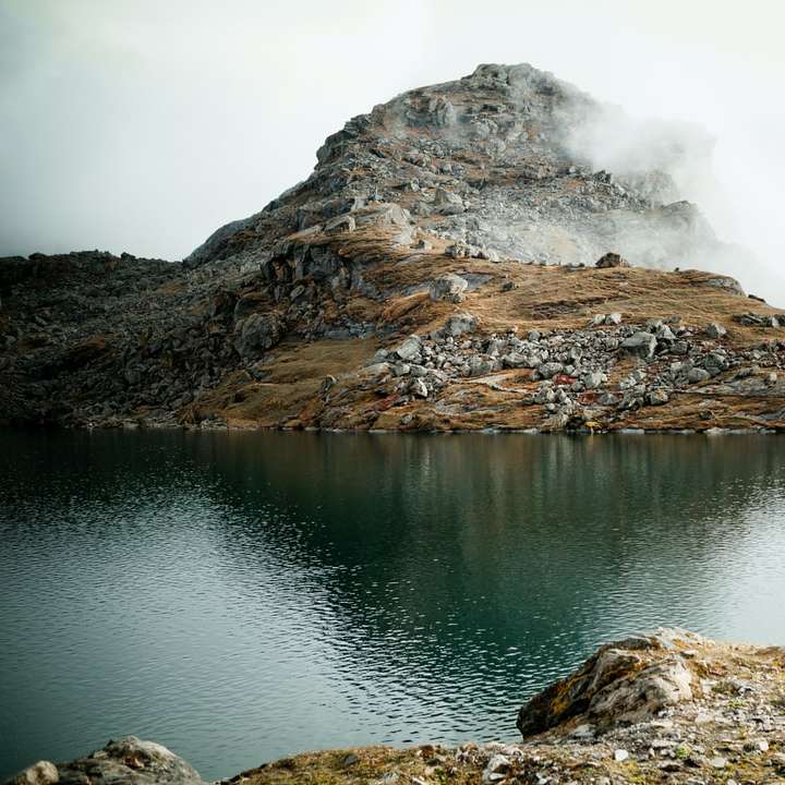 Hnědá skalnatá hora vedle jezera pod bílou oblohu posuvné puzzle online