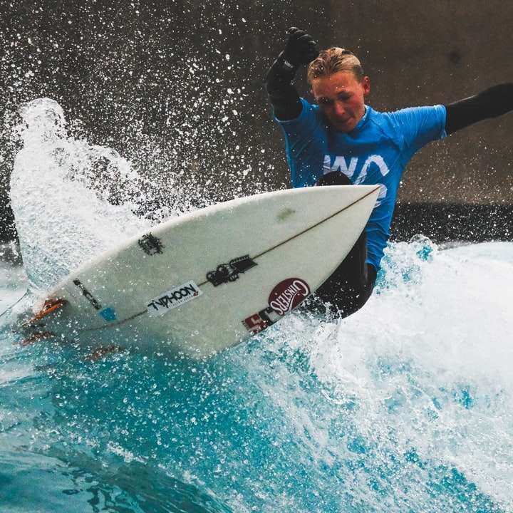 Mann im blauen und weißen nassen Anzug, der weiße Surfbrett hält Online-Puzzle