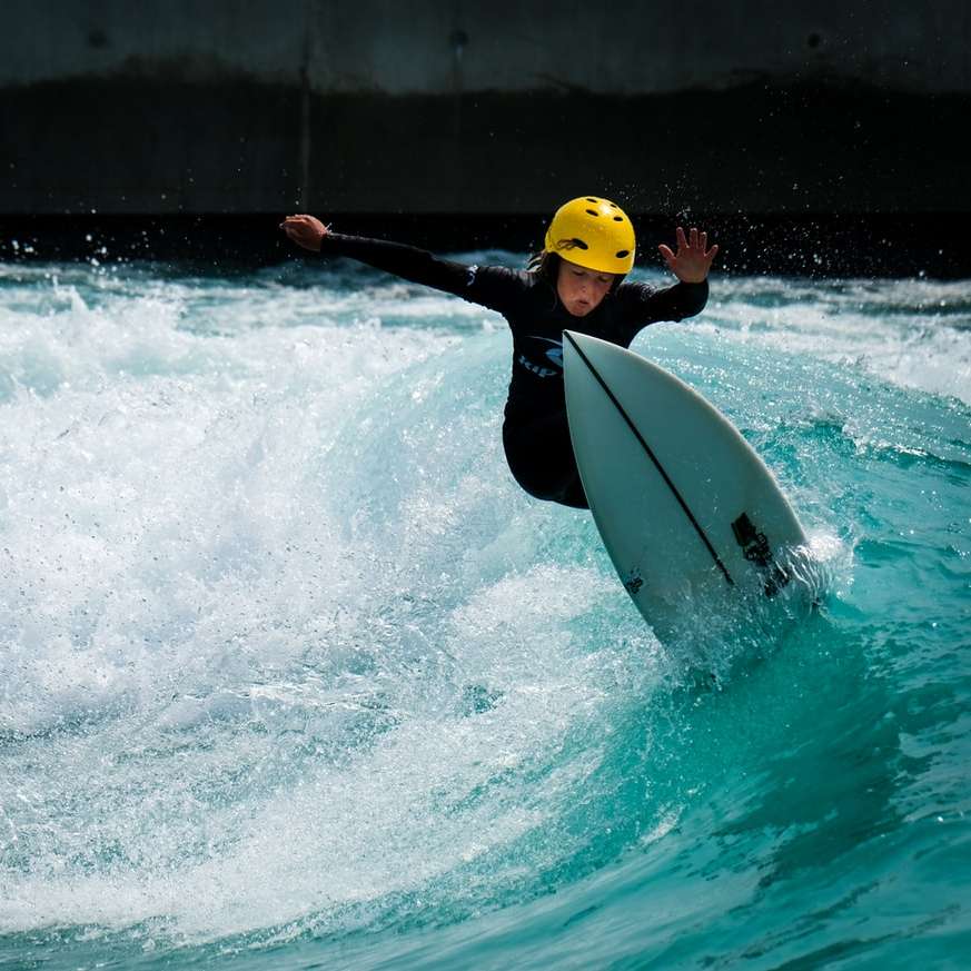 Ο άνθρωπος σε μαύρο wetsuit που οδηγεί λευκή σανίδα στο νερό συρόμενο παζλ online