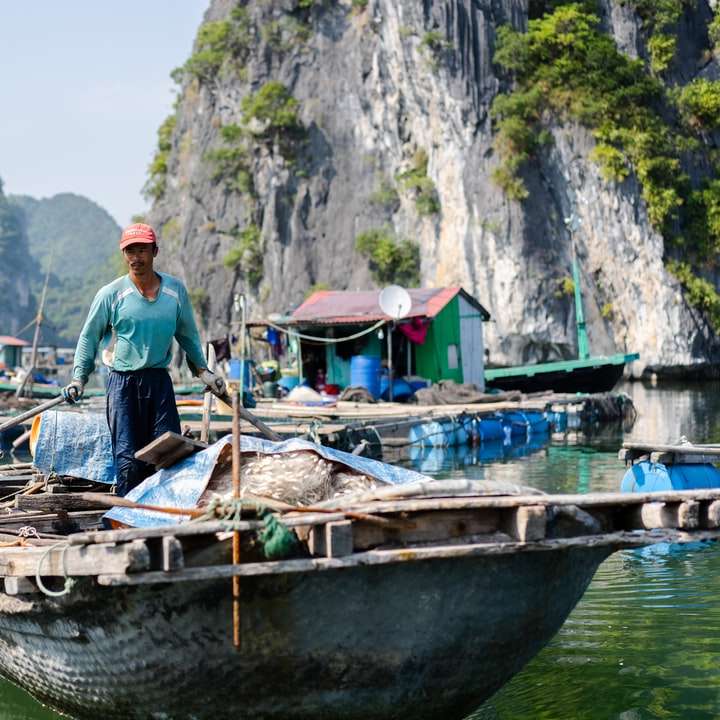 Ο άνθρωπος σε μπλε πουκάμισο στέκεται στη βάρκα στο ποτάμι κατά τη διάρκεια της ημέρας συρόμενο παζλ online