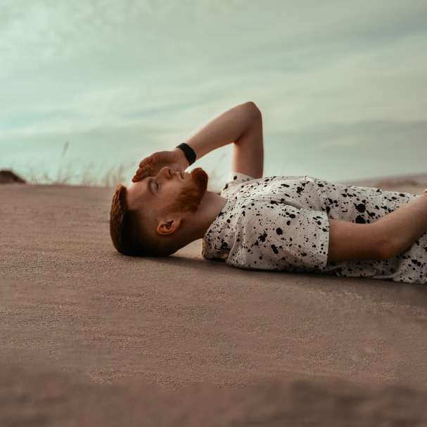 Kvinna i vit och svart blommig klänning som ligger på brun sand Pussel online