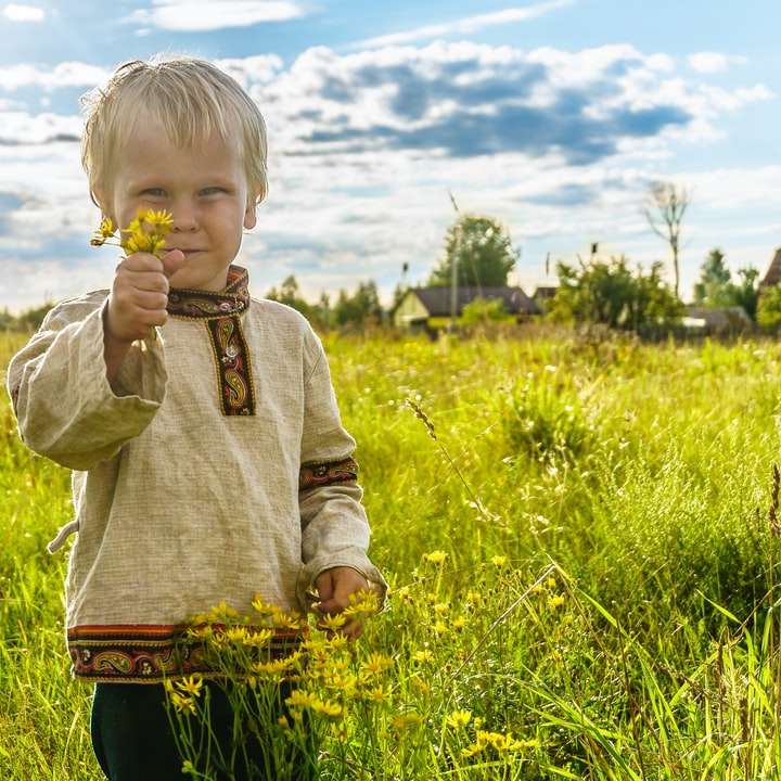 Chłopiec w szarym sweter pozyci na zielonej trawy polu puzzle przesuwne online