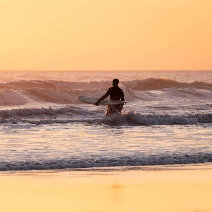 Az ember szörfözés a tenger hullámaiban naplementekor online puzzle