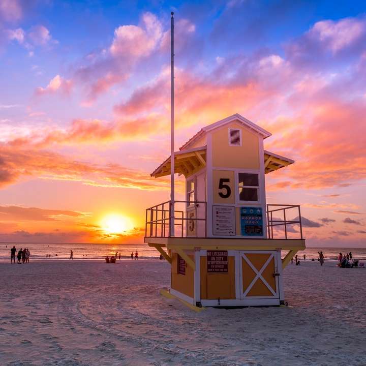 Casa de salvavidas de madera blanca en la playa durante la puesta del sol rompecabezas en línea