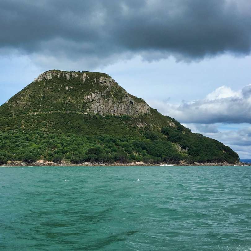 Zielona góra obok ciała wody pod zachmurzonym niebem puzzle przesuwne online