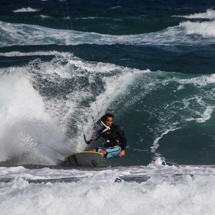 Omul în costum umed negru de echitatie galben Surfboard pe valuri de mare alunecare puzzle online