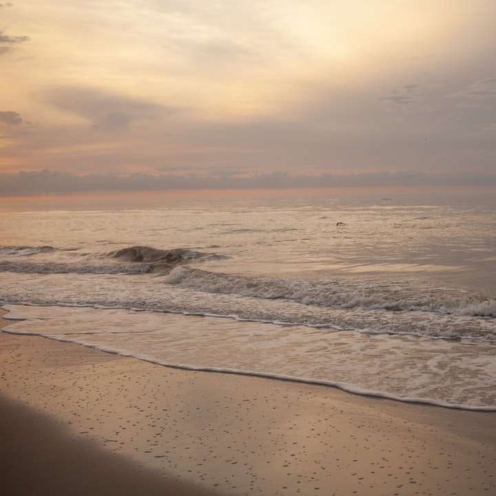Havsvågor kraschar på stranden under solnedgången Pussel online