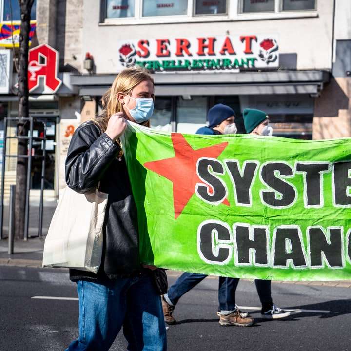 жена в черно яке, държащо зелен банер онлайн пъзел
