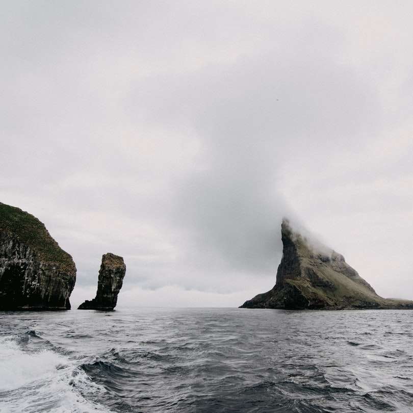 Hnědá skalní útvar na moři pod bílými mraky posuvné puzzle online