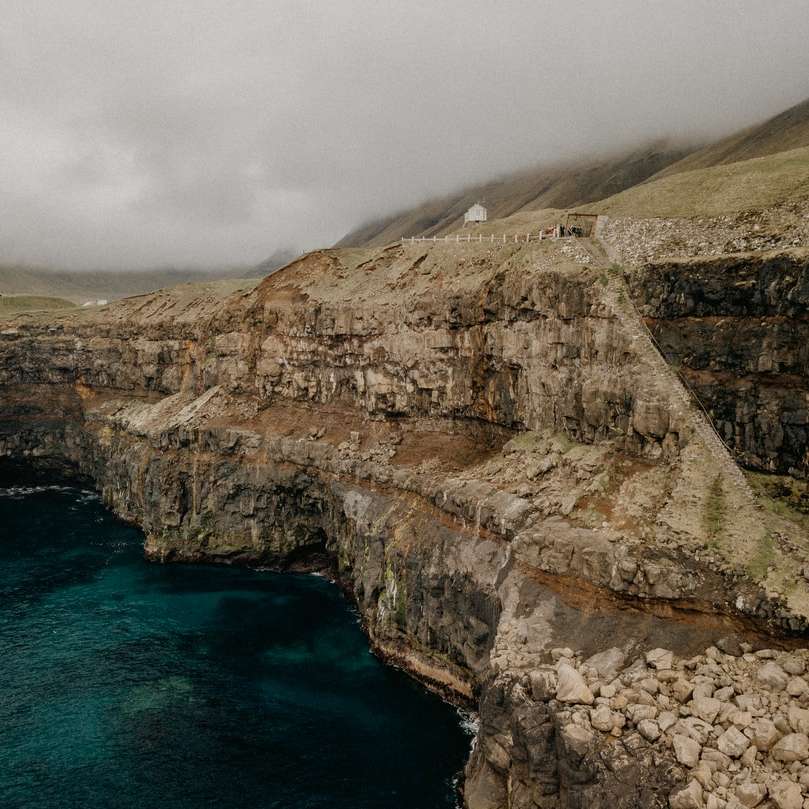 Montagna rocciosa marrone al lato del mare blu sotto le nuvole bianche puzzle online