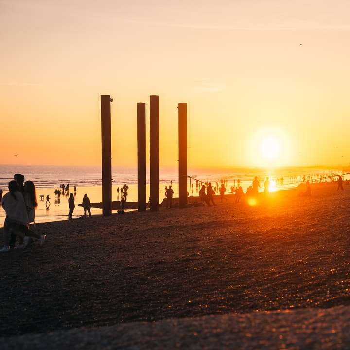 Silueta de personas que caminan en la playa durante la puesta del sol puzzle deslizante online