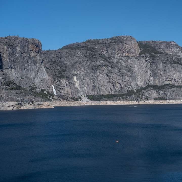 сіра скеляста гора біля синього моря під блакитним небом розсувний пазл онлайн