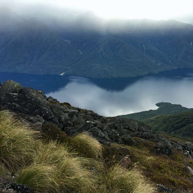 Muntele verde și maro de lângă lac în timpul zilei alunecare puzzle online