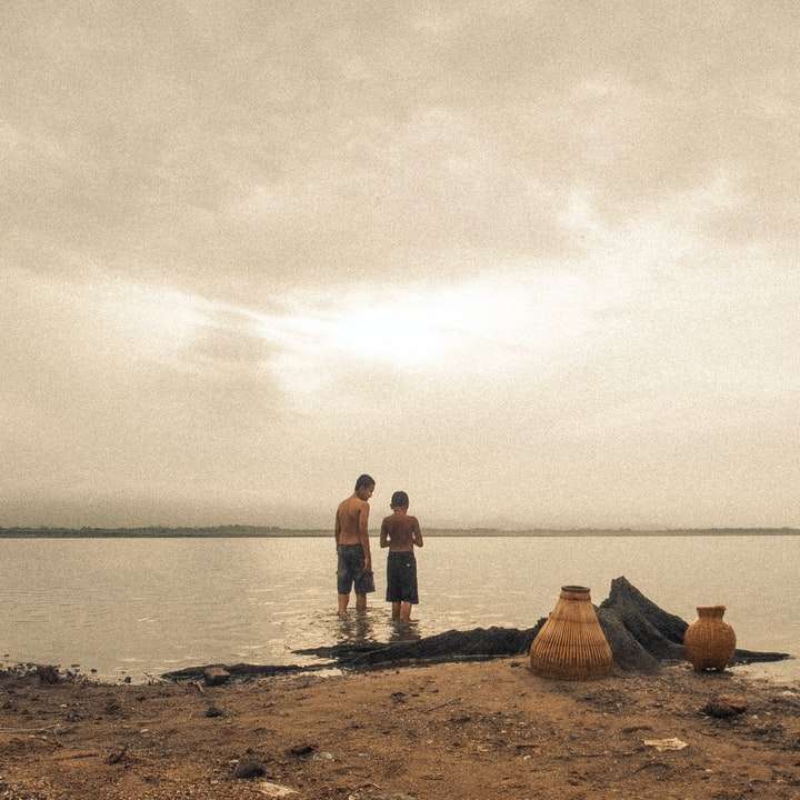 Ludzie stojący na brązowym piasku w pobliżu wody puzzle przesuwne online