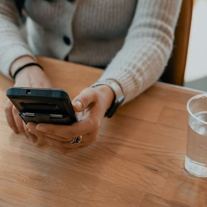Frau im weißen Pullover, der schwarze Smartphone hält Online-Puzzle