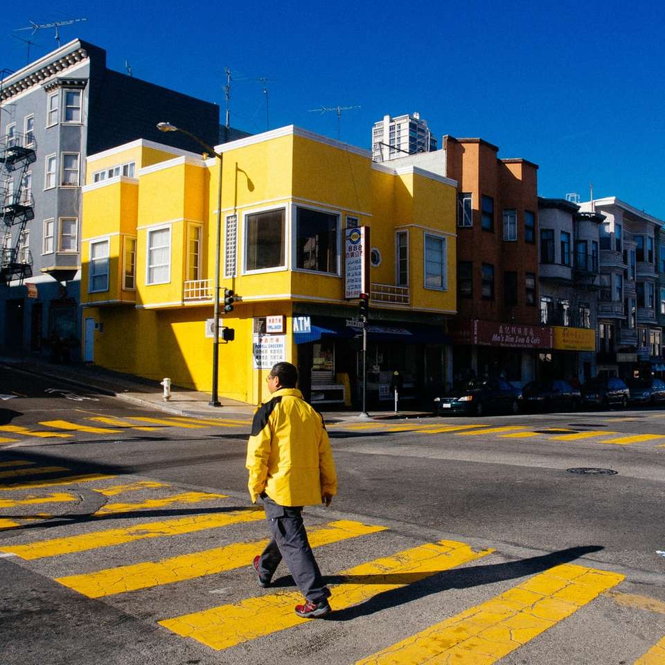 Person in der gelben Jacke, die während der Tageszeit auf Bürgersteig geht Online-Puzzle