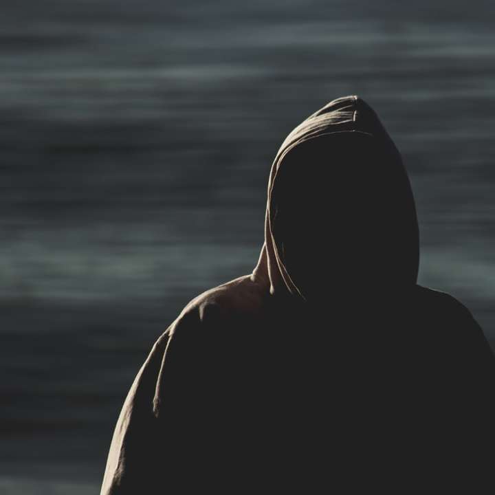 person in black hoodie standing near body of water sliding puzzle online