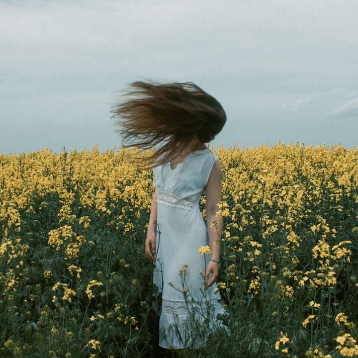 женщина в белом платье стоит на желтом цветочном поле онлайн-пазл