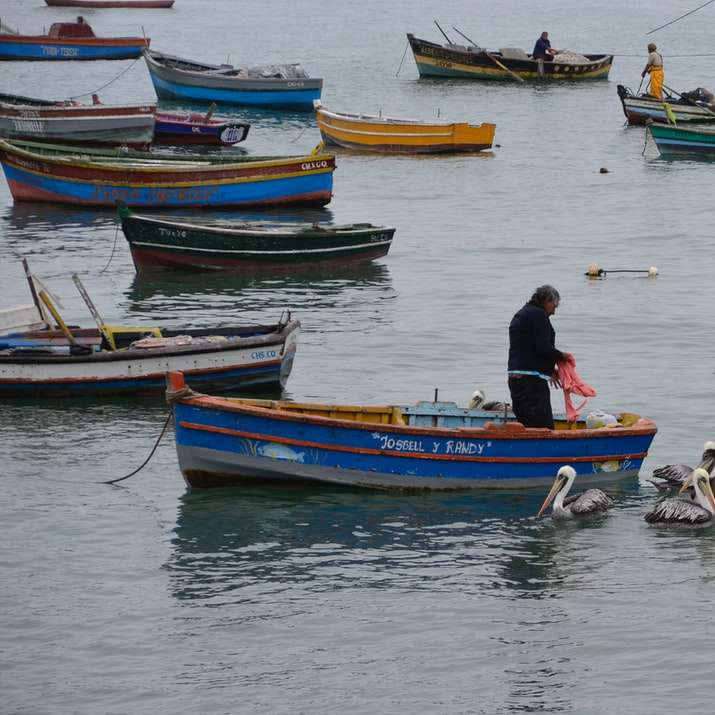Mann in der schwarzen Jacke, die auf rotem und blauem Boot auf Wasser reitet Online-Puzzle