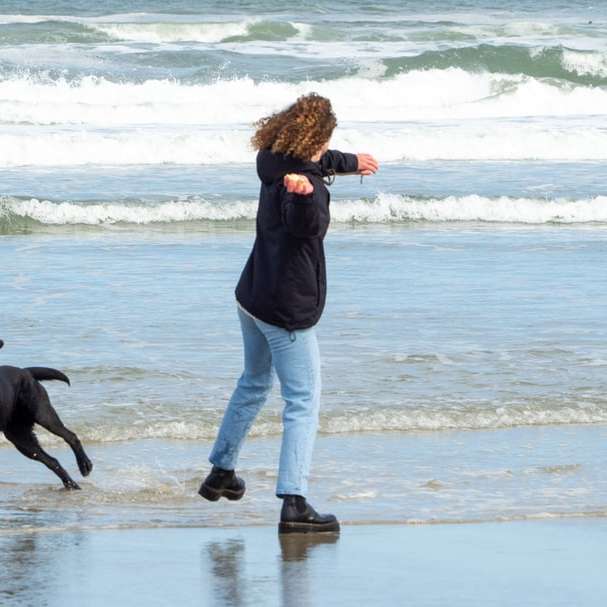 Kobieta w czarnej kurtce i białych spodniach spaceru na plaży puzzle online