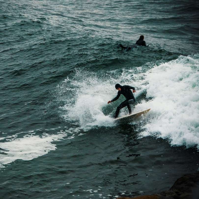 Homme en costume mouillé rouge et noir surfer sur les vagues de la mer puzzle en ligne