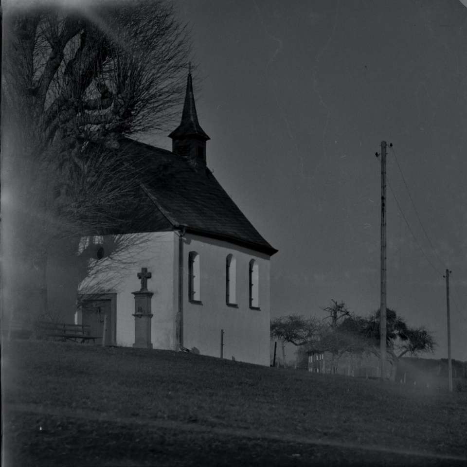 Grayscale fotografie de biserică lângă copaci gați alunecare puzzle online