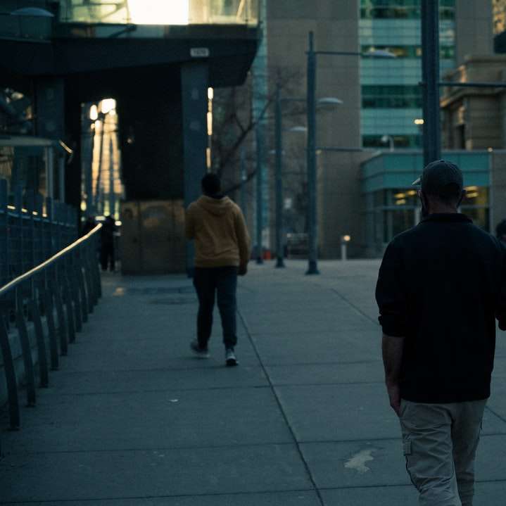 Man i svart skjorta och gråbyxor som går på trottoaren Pussel online