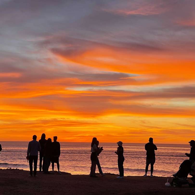 Silueta de personas de pie en la playa durante la puesta del sol puzzle deslizante online