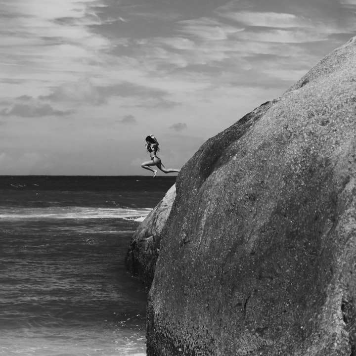 Skala szarości Zdjęcie człowieka siedzi na skale w pobliżu morza puzzle online