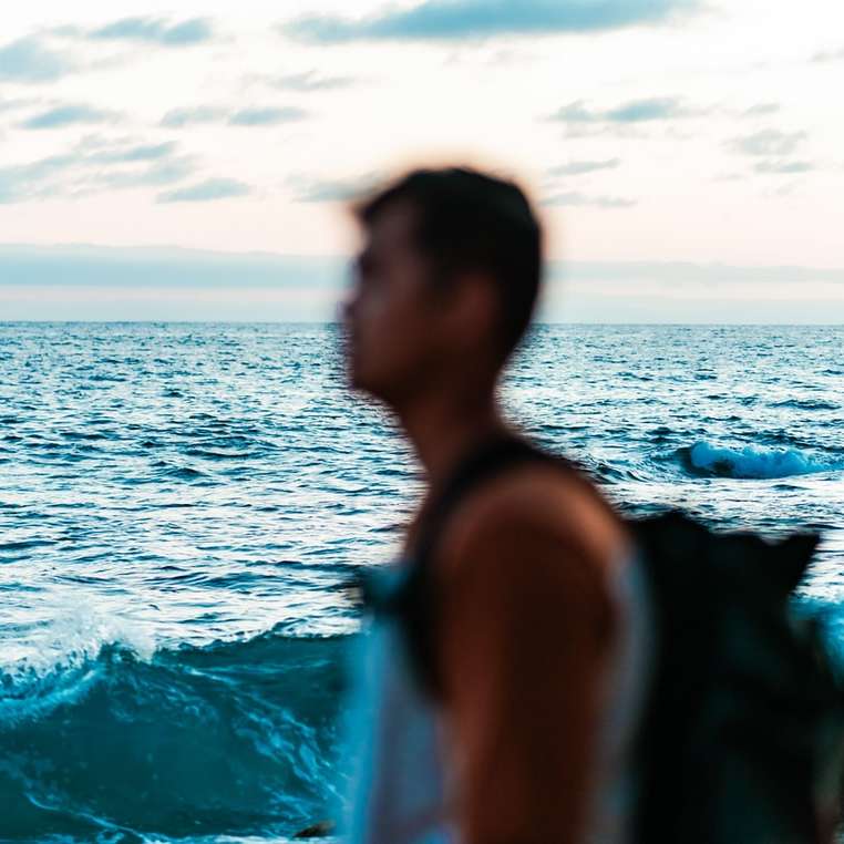Жена в бял резервоар, който стои на море през деня онлайн пъзел