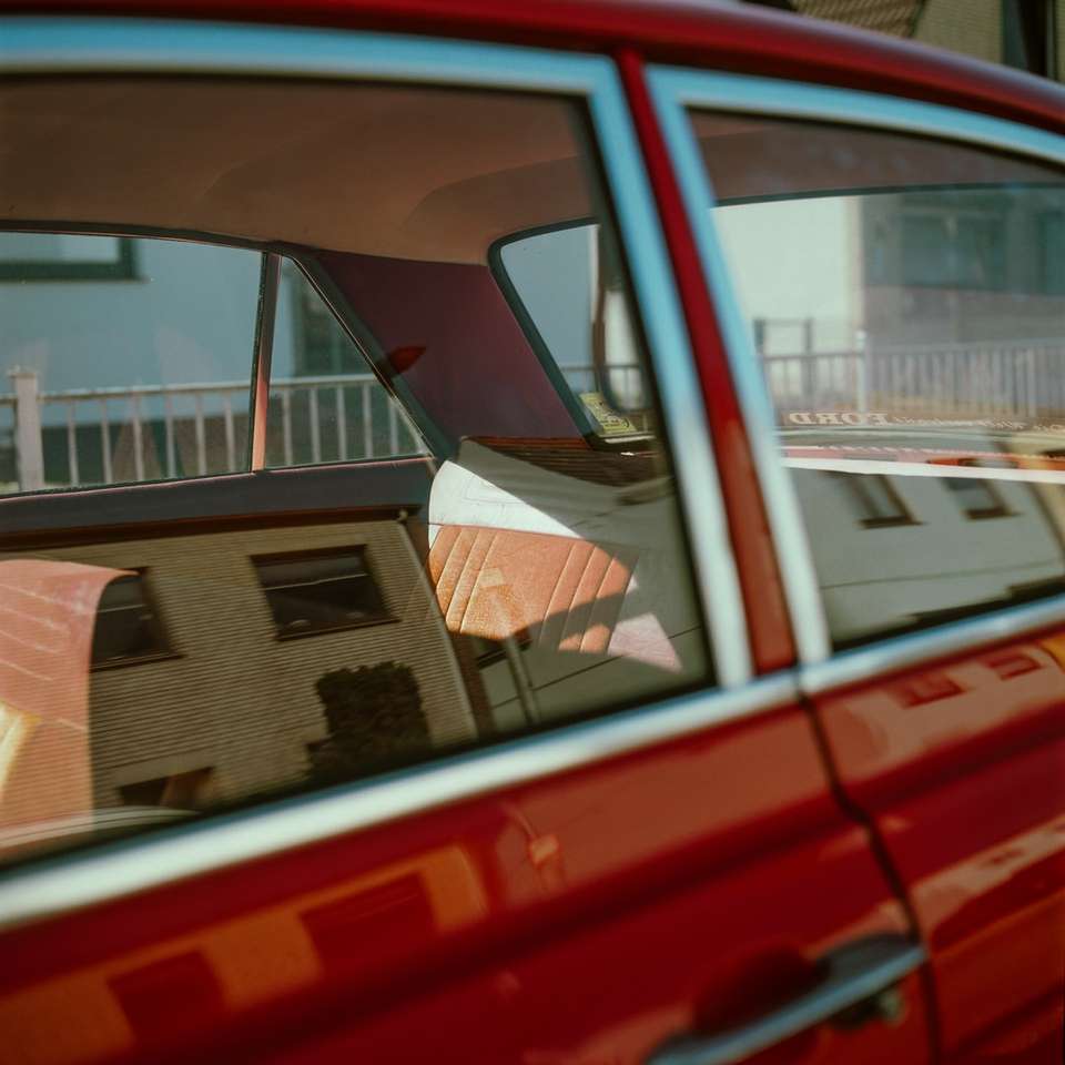 Rotes Auto geparkt in der Nähe von weißem Betongebäude tagsüber Online-Puzzle