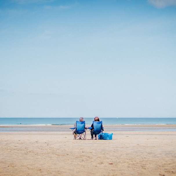 2 persona che si siede sulla sabbia della spiaggia durante il giorno puzzle scorrevole online