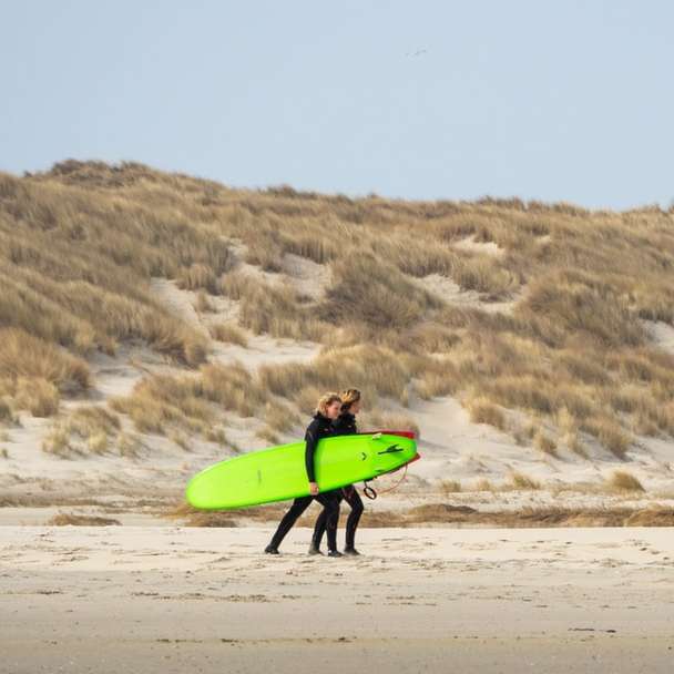 Omul în sacou albastru care deține bordul verde de surf alunecare puzzle online