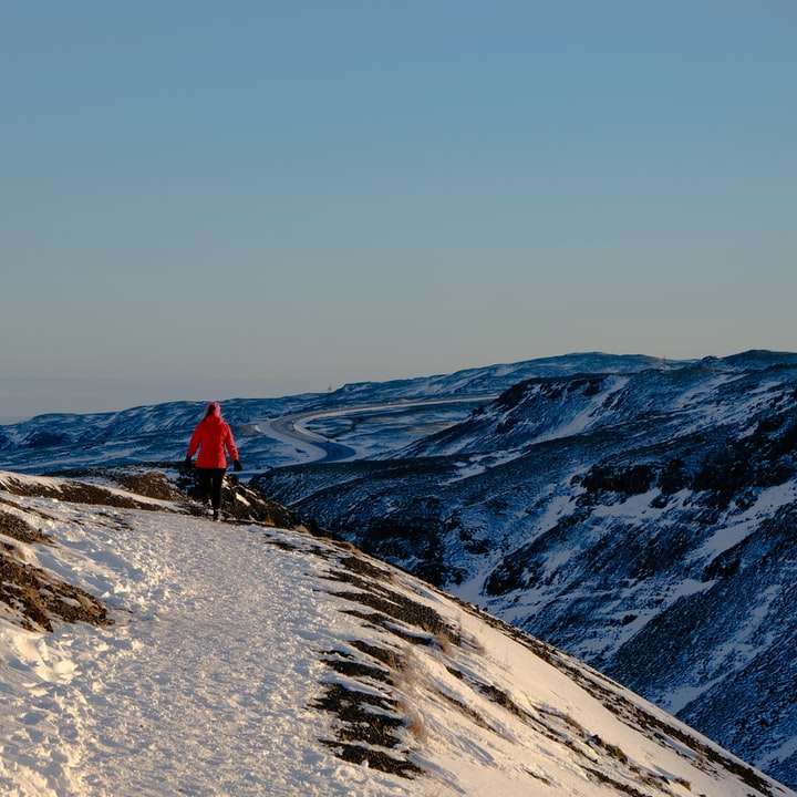 Persona en chaqueta roja caminando en la montaña cubierta de nieve rompecabezas en línea