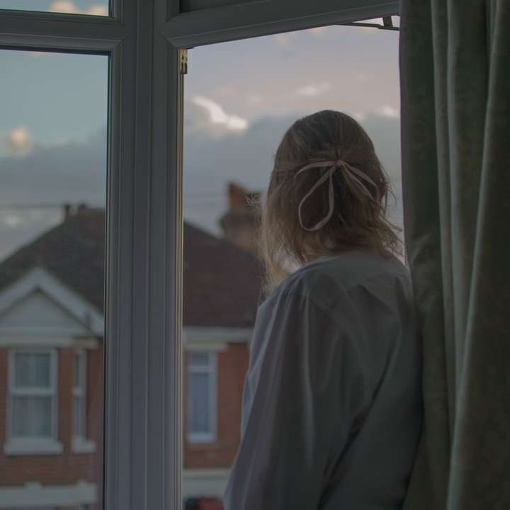woman in gray coat standing near window sliding puzzle online