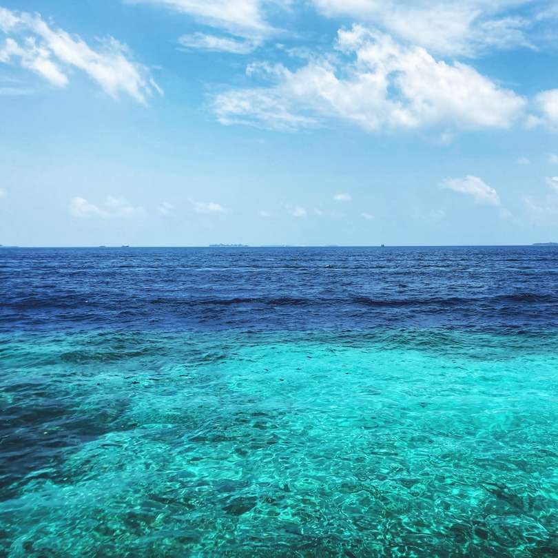 Mar azul sob céu azul e nuvens brancas durante o dia puzzle deslizante online