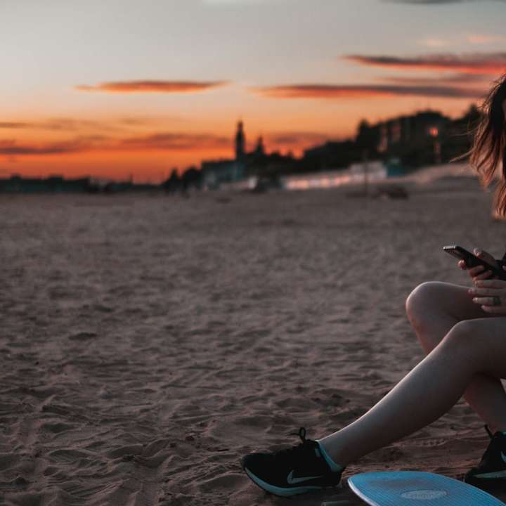 Kobieta w czarnej koszuli i niebieskich dżinsach siedzi na plaży puzzle przesuwne online