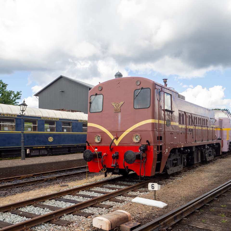Treno blu e rosso sulle tracce ferroviarie sotto il cielo nuvoloso puzzle scorrevole online