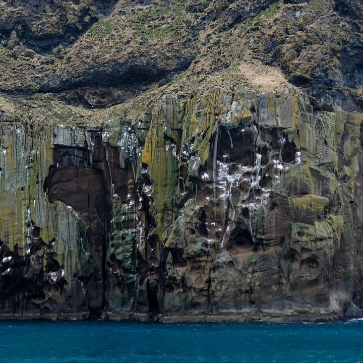 Formación rocosa marrón y verde junto al mar azul rompecabezas en línea