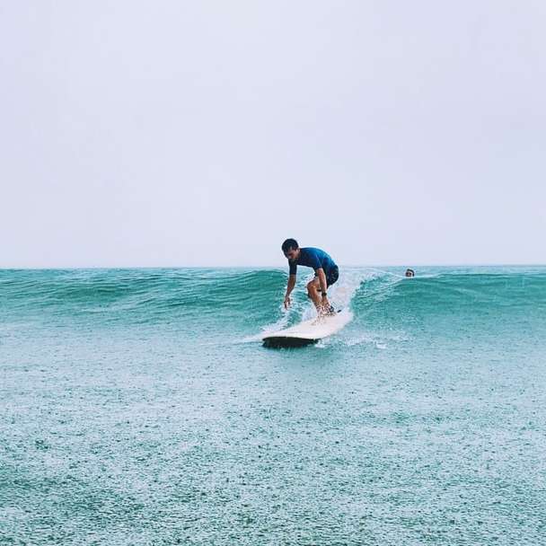 mężczyzna w niebieskiej koszuli i czarnych spodenkach jedzie na białej desce surfingowej puzzle przesuwne online