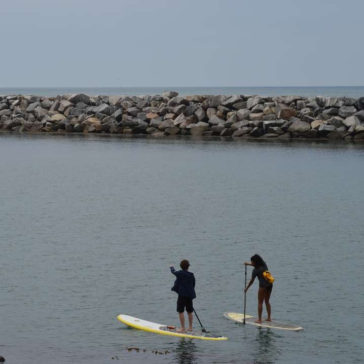 мъж и жена в черен мокър костюм, каращи жълта дъска за сърф плъзгащ се пъзел онлайн