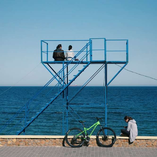 мъж с бяла риза и черни панталони, седнал на син велосипед плъзгащ се пъзел онлайн