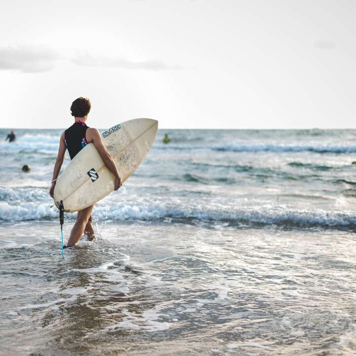 homme en combinaison noire portant une planche de surf blanche puzzle en ligne