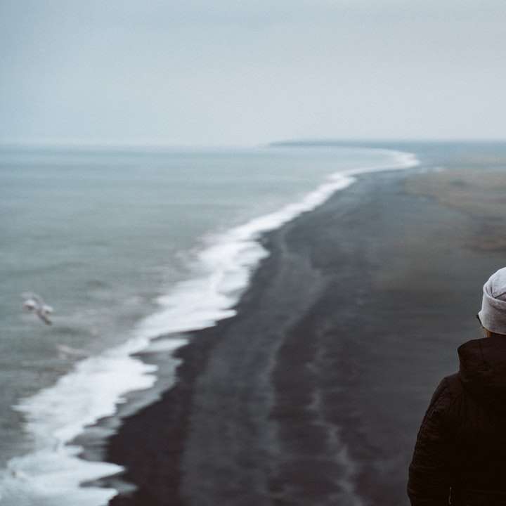 osoba w czarnej kurtce stojąca nad brzegiem morza w ciągu dnia puzzle online