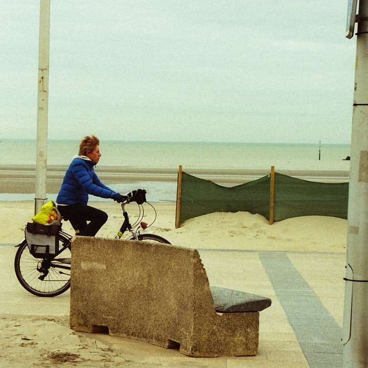 мъж в синьо яке, каращ черен мотоциклет на плажа плъзгащ се пъзел онлайн