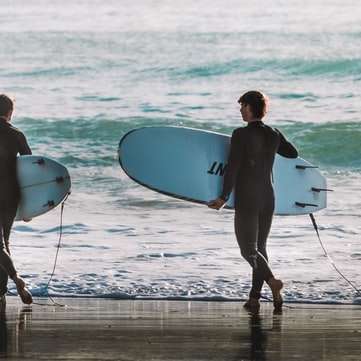 мъж и жена, държащи бяла дъска за сърф, разхождайки се по плажа онлайн пъзел