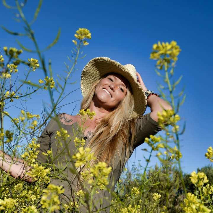 κορίτσι με καφέ καπέλο ηλίου που στέκεται στο πεδίο κίτρινων λουλουδιών online παζλ