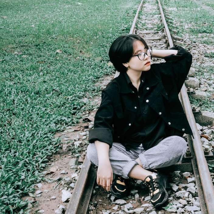 Frau in schwarzer Jacke, die tagsüber auf der Zugschiene sitzt Schiebepuzzle online