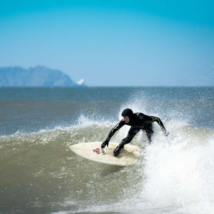 Hombre en traje de neopreno negro surfeando en el mar durante el día rompecabezas en línea