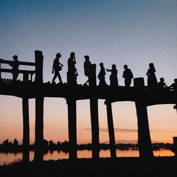 sylwetka ludzi stojących na drewnianym pomoście podczas zachodu słońca puzzle przesuwne online